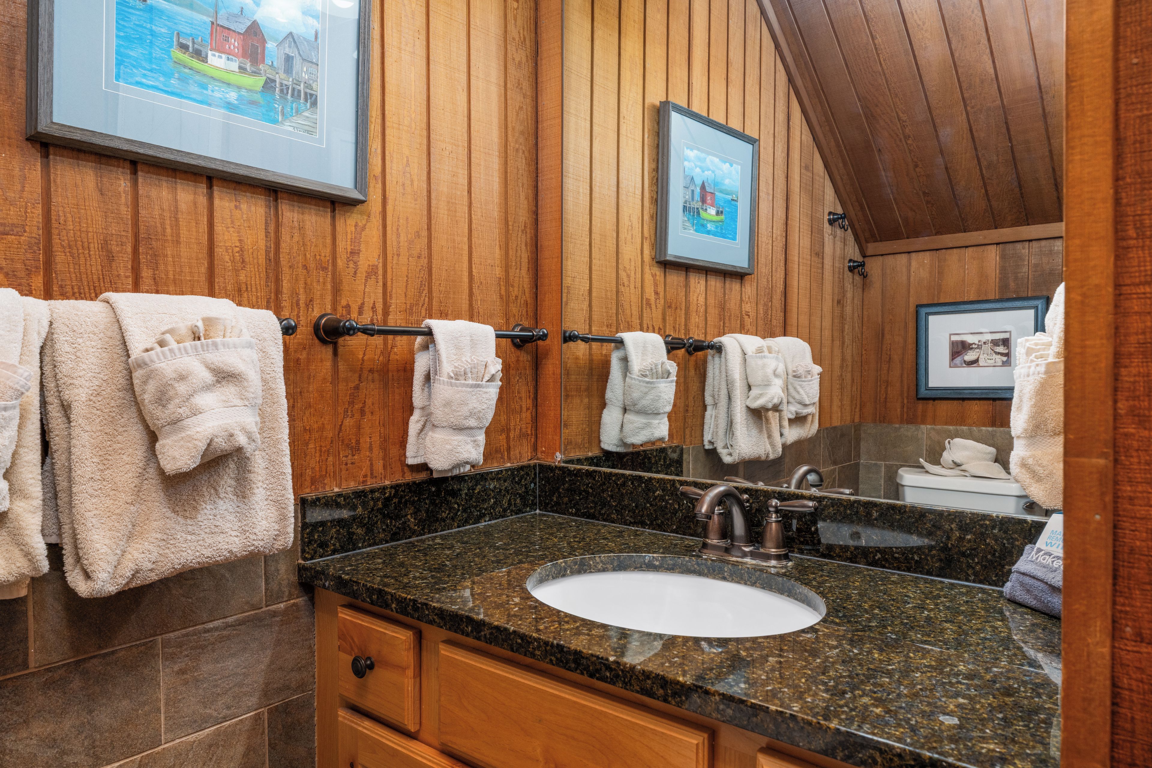 A bathroom with wooden paneling, a granite countertop, a sink, and multiple towels hanging on a rack.