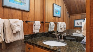 Baño con paneles de madera, encimera de granito, lavamanos y varias toallas colgadas en un perchero.