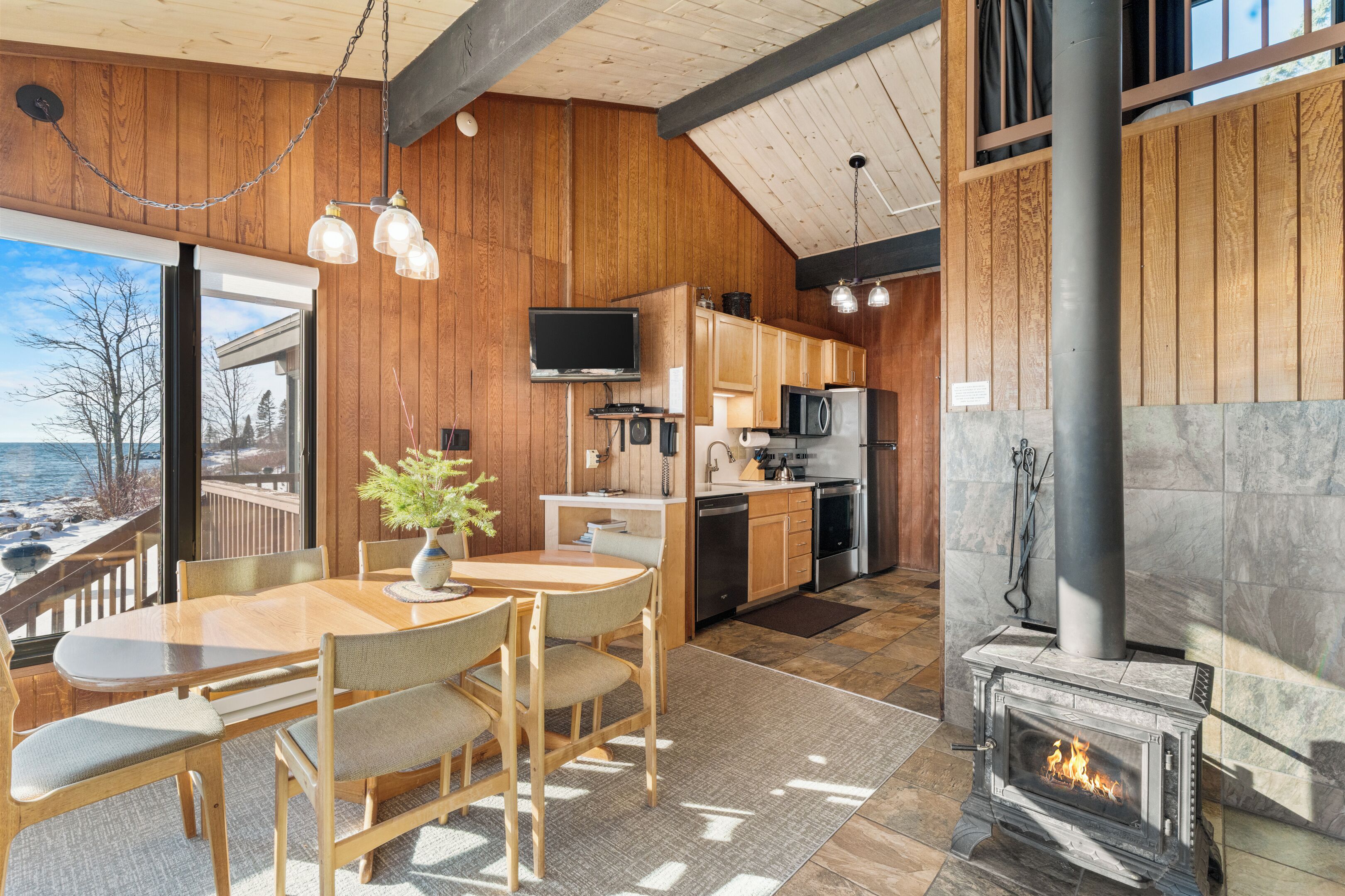 A wooden interior with a dining area, kitchen, and fireplace.