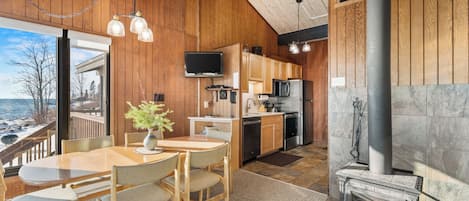 A wooden interior with a dining area, kitchen, and fireplace.