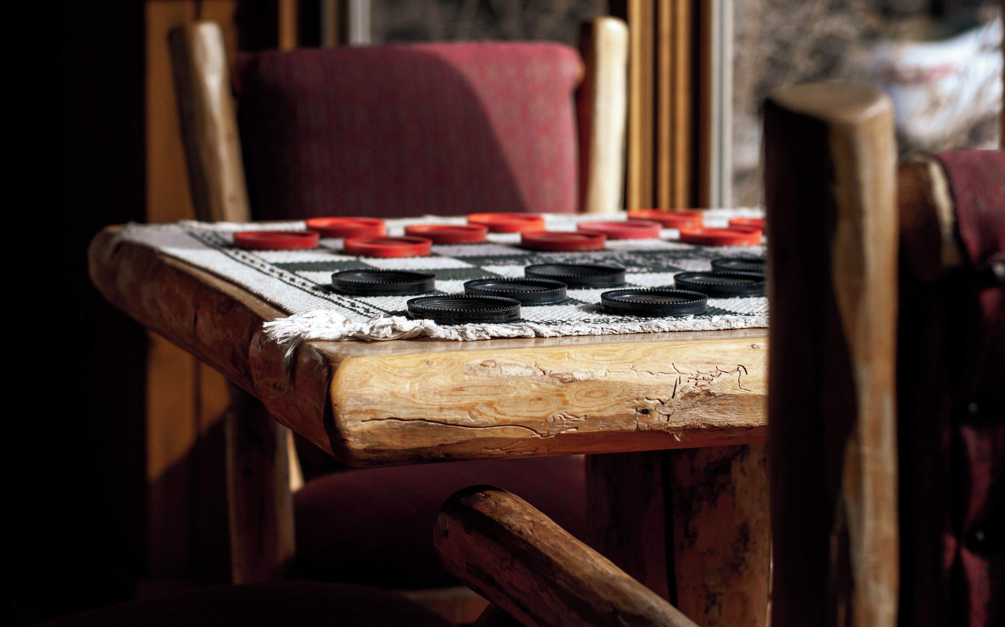 A close-up of a wooden table with a checkered cloth, featuring black and red game pieces.