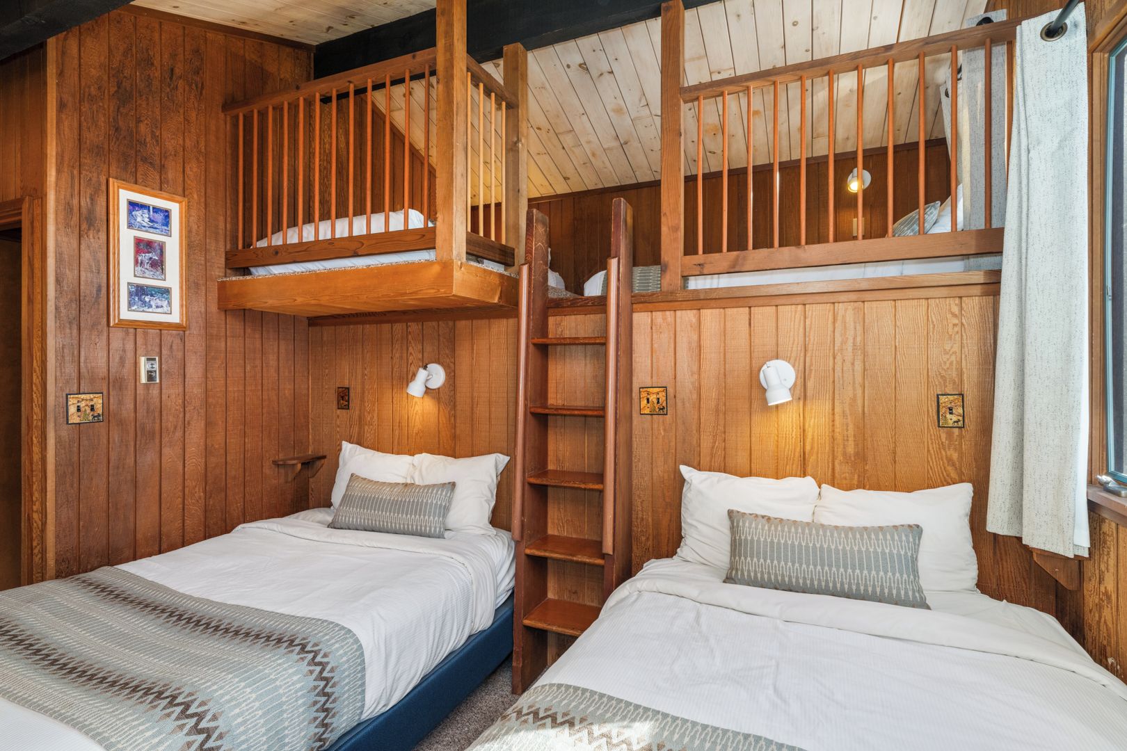 A cabin-style bedroom with two beds, wooden walls, and a loft bed.