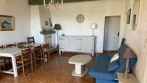 Zona pranzo con tavolo e sedie, un divano, una lampada e un orologio appeso al muro.