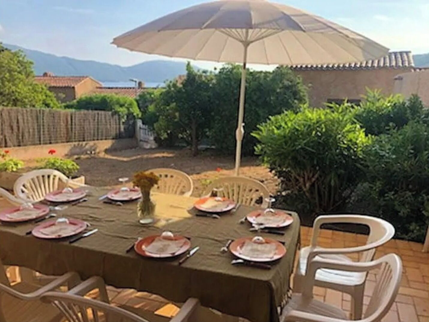 An outdoor dining area with a table set for four, surrounded by chairs, under a large umbrella.