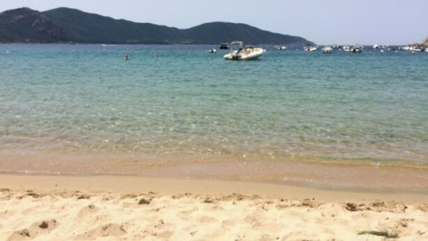 Una spiaggia con acque limpide, barche e montagne sullo sfondo.