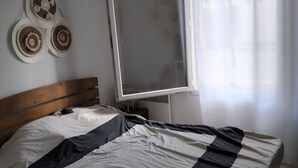 Et soveværelse med en seng, et vindue med lette gardiner, et spejl på væggen og en vægdekoration.