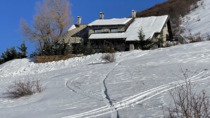 A stone house with a sloped roof, surrounded by snow-covered ground and trees.