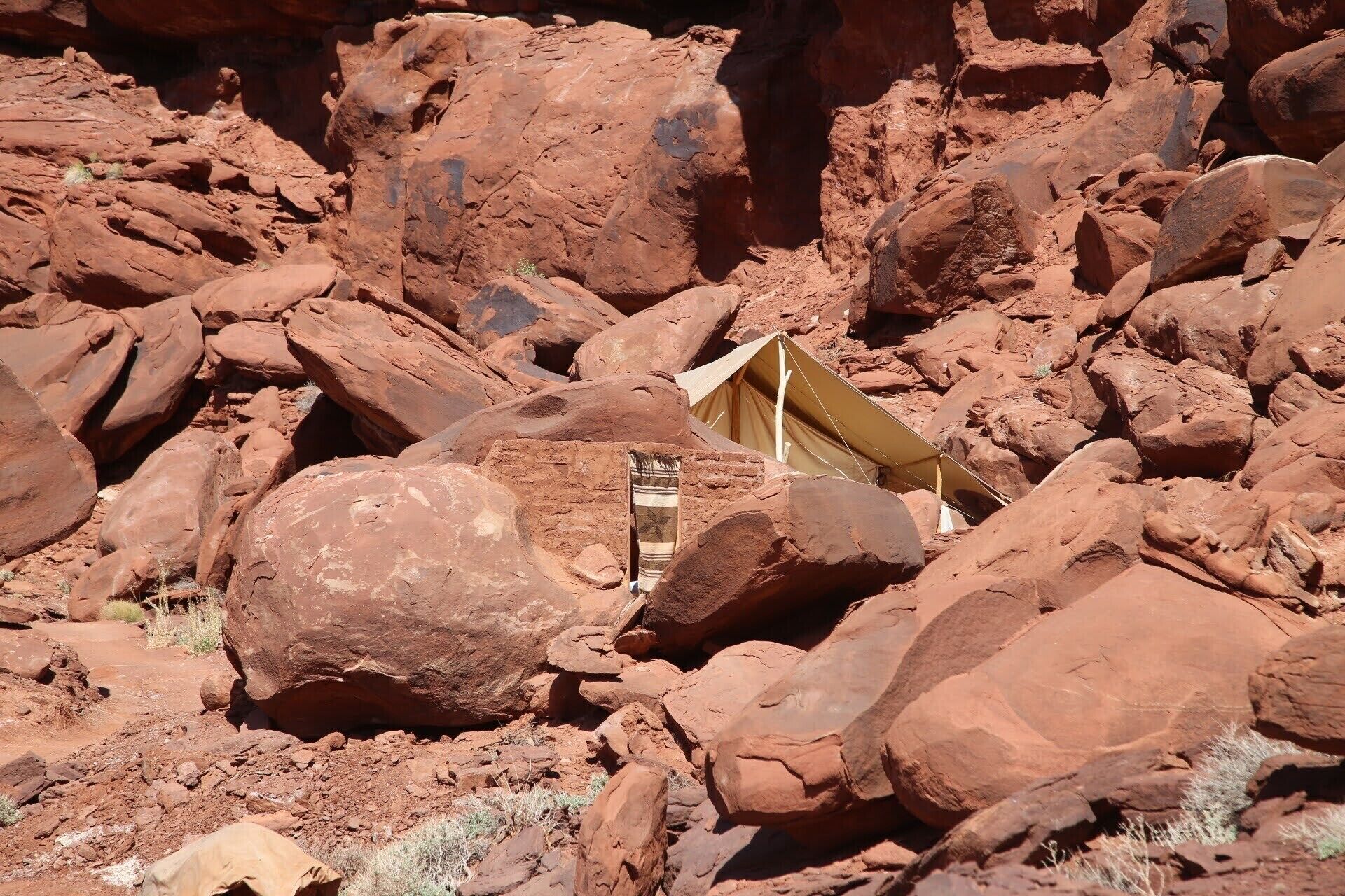 A tent set up among red rocks, surrounded by large boulders.