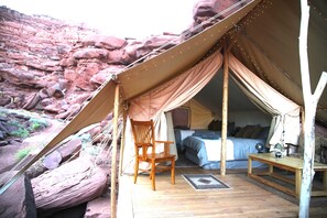 A tented accommodation with a bed, a chair, and a small table.