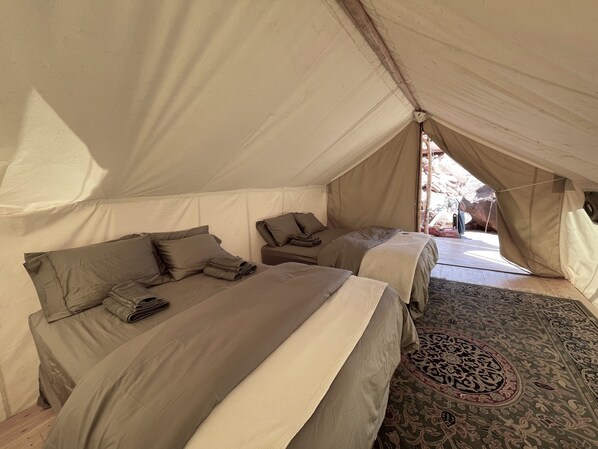 A tented accommodation with two beds, a patterned rug, and a view of the outdoors.