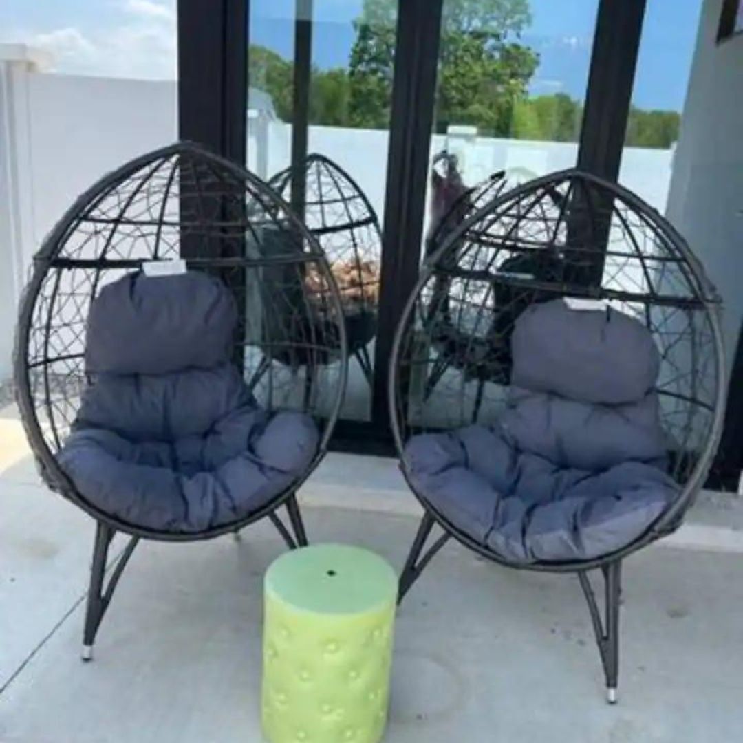 Two hanging chairs with cushions, a small green stool, and a glass table.