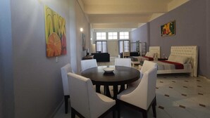 A spacious living room with a dining area, featuring a round table and white chairs, a sofa, and artwork on the walls. - Amplio estudio en Cozumel, frente al mar E12 (San Miguel de Cozumel)