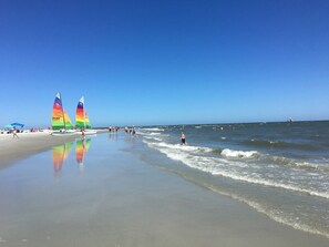 Une plage avec des voiliers, des gens qui se promènent et l’océan.