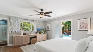 Un dormitorio con cama, escritorio, ventilador de techo y vista a una piscina.