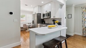 Una cocina moderna con armarios blancos, una isla central, un refrigerador, un microondas y una estufa.