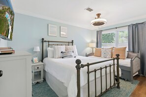 Une chambre à coucher comprenant un lit, des tables de chevet, une commode, une lampe, un cadre photo et une fenêtre avec des rideaux.