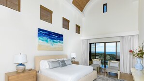 Un dormitorio amplio con una cama grande, un cuadro del océano y un balcón con vistas.