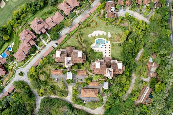 An aerial view of a residential area with multiple houses, a swimming pool, and well-maintained gardens.