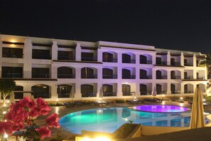 Un hotel con una piscina amplia, varios balcones y zonas de estar al aire libre.