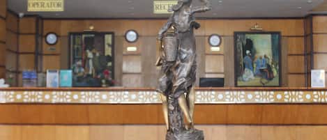 Un espace d’accueil agrémenté d’une statue représentant une femme tenant un panier, de panneaux de bois, d’horloges et d’œuvres d’art encadrées accrochées aux murs.