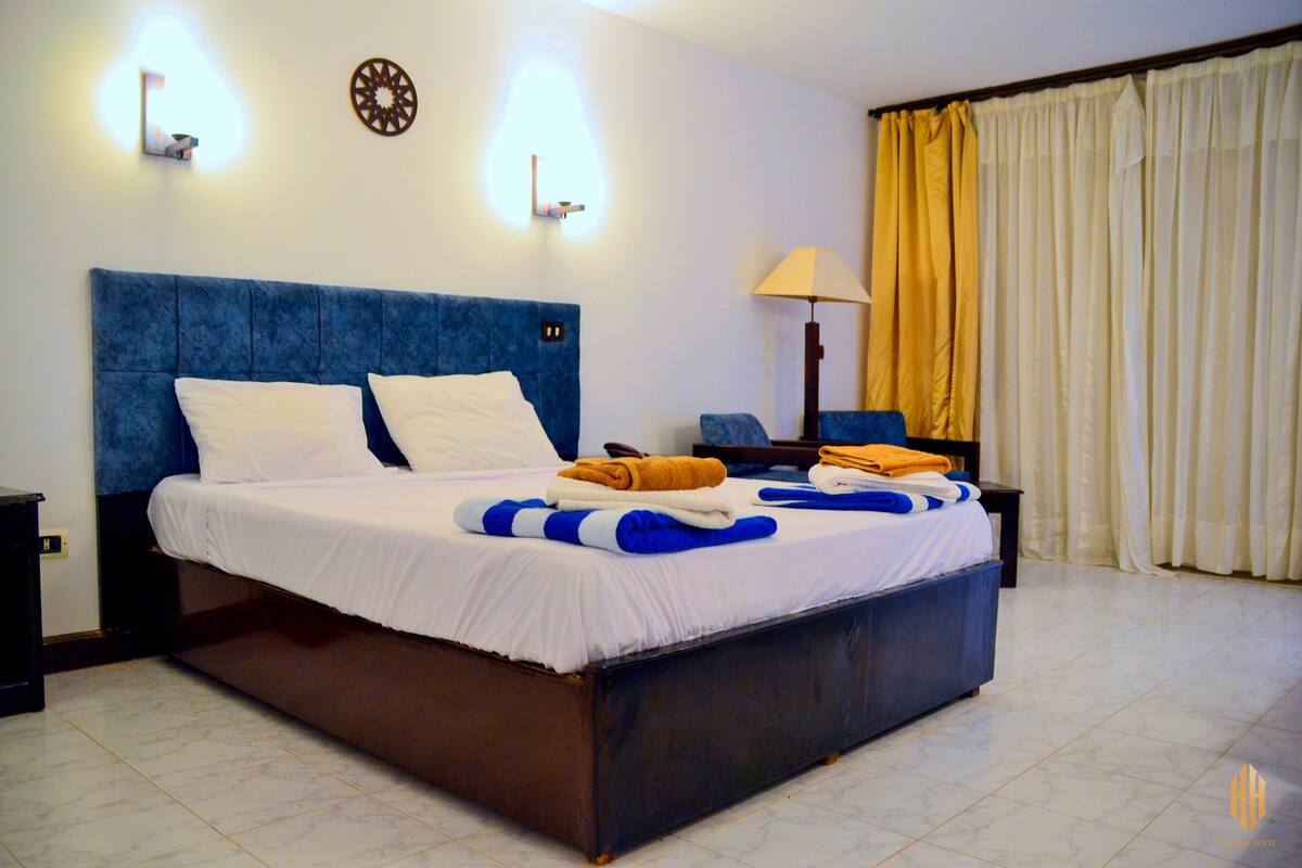 A neatly made bed with white and blue bedding, a blue headboard, and a bedside table with a lamp.