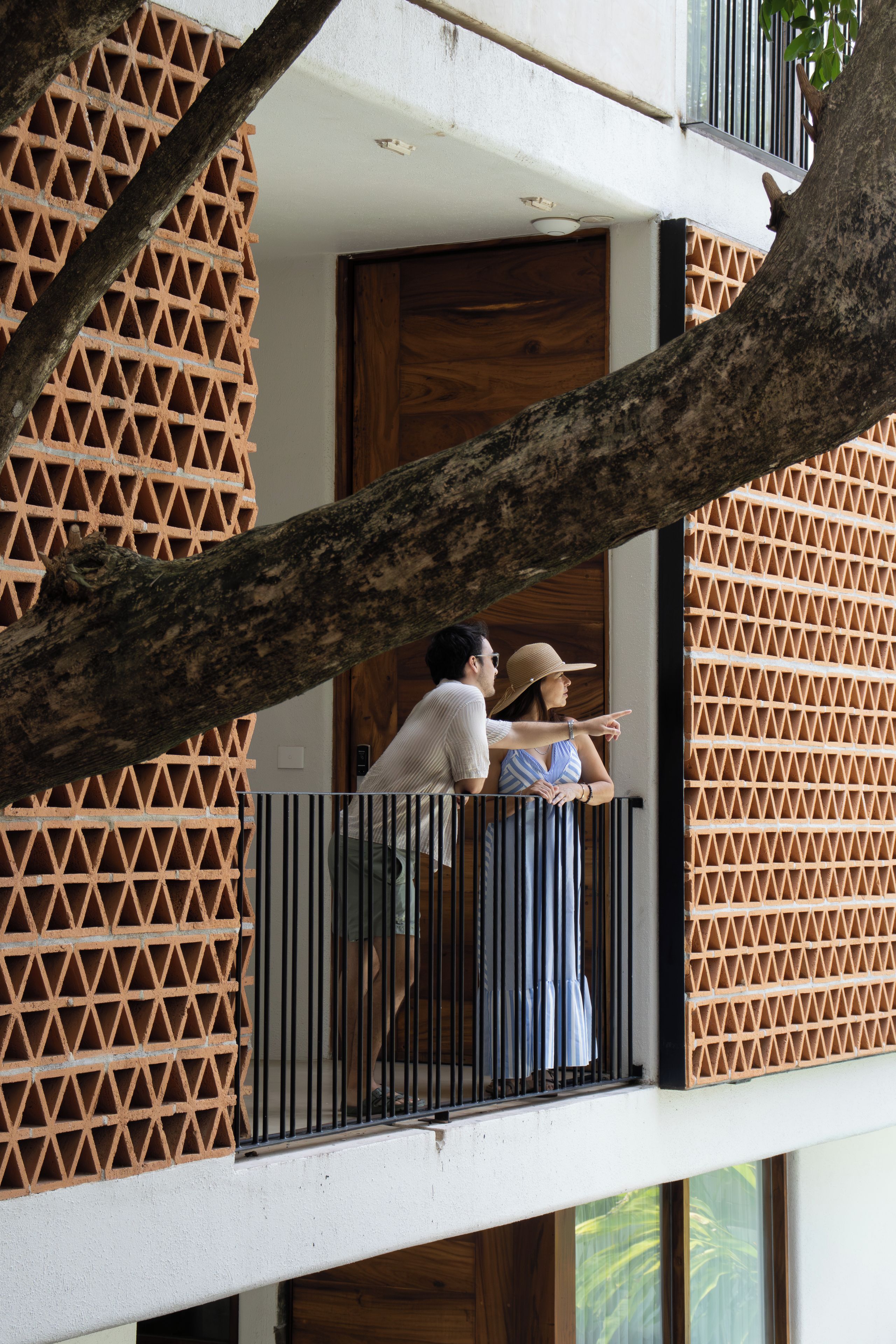 Un balcon avec un mur orné d’un motif géométrique, une porte en bois et une branche d’arbre qui obstrue partiellement la vue.
