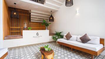 Un área de recepción con un mostrador de madera, un sofá con cojines, un banco de madera y lámparas colgantes.