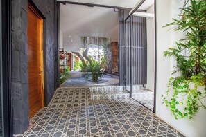 A hallway with a patterned floor, a wooden door, and a plant on the right.