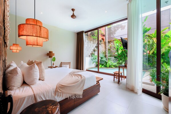 Un dormitorio moderno con una cama grande, un escritorio y vistas a una piscina y follaje.