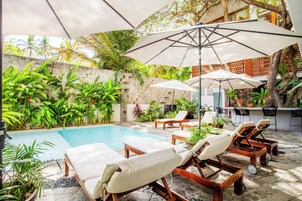 Zona junto a la piscina con sillones, sombrillas y un bar con asientos.