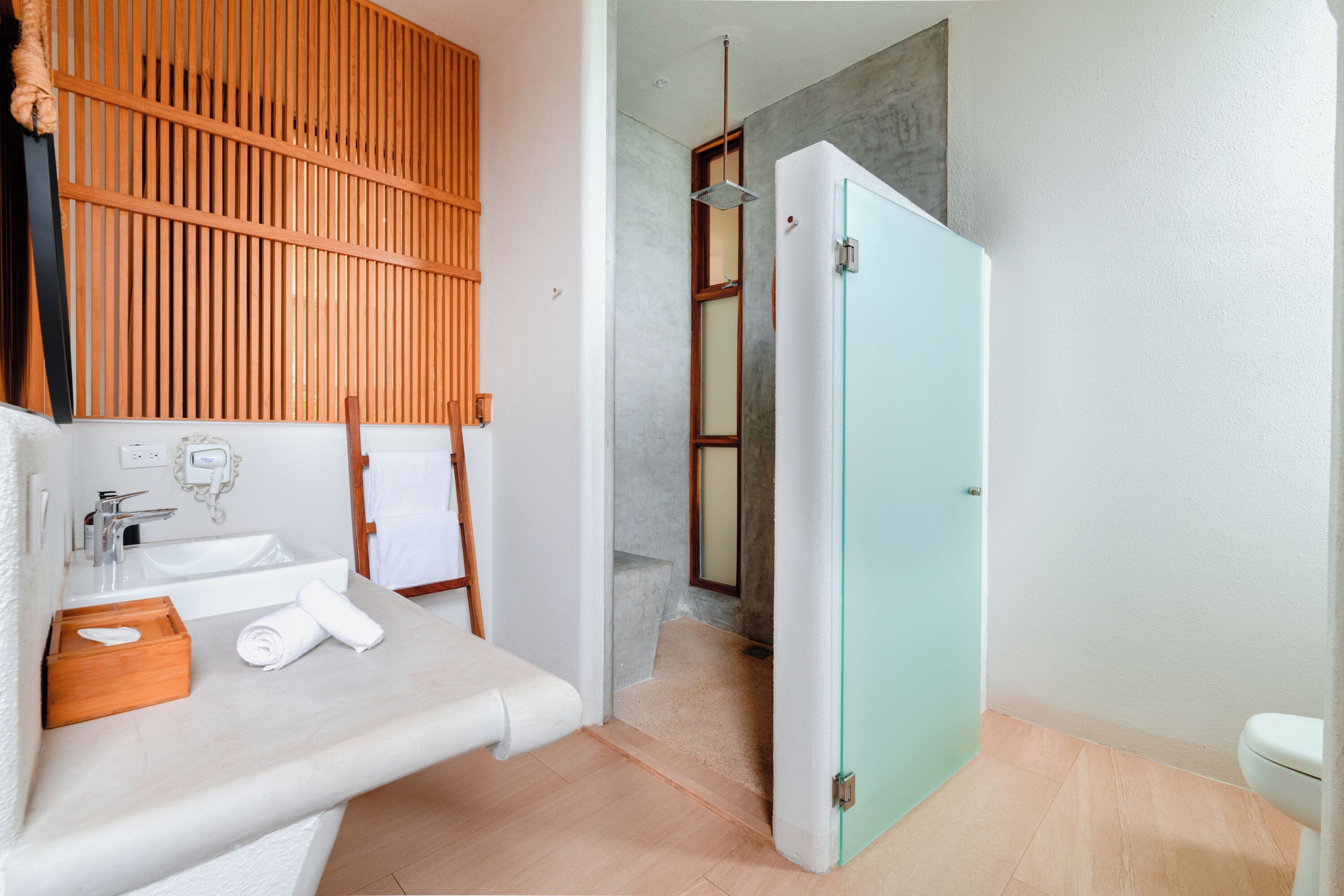 A bathroom with a sink, towel, wooden slat wall, and a door leading to a shower area.