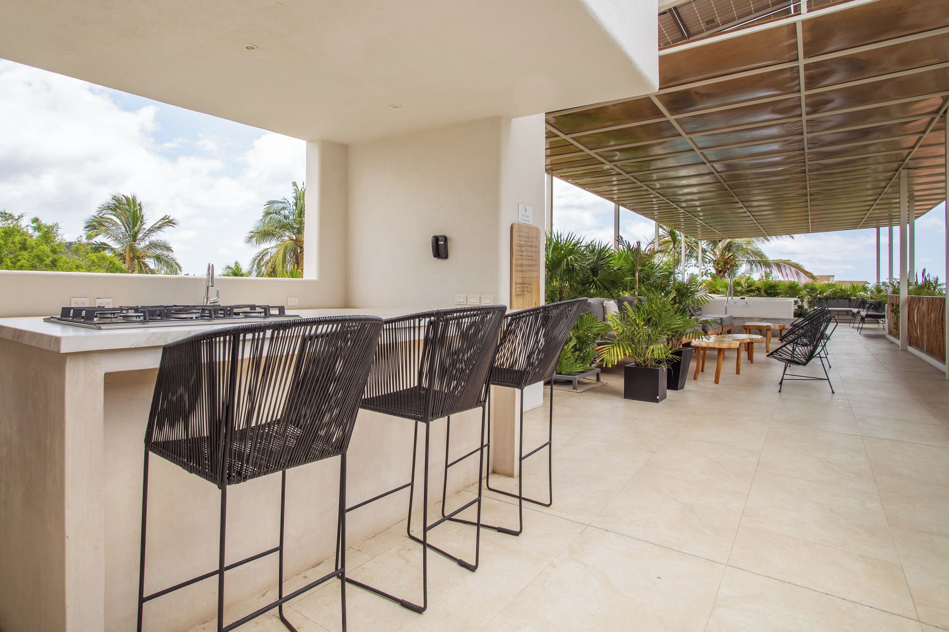 An outdoor patio with a bar area, black metal chairs, and a mix of wooden and metal tables.