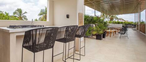 An outdoor patio with a bar area, black metal chairs, and a mix of wooden and metal tables.