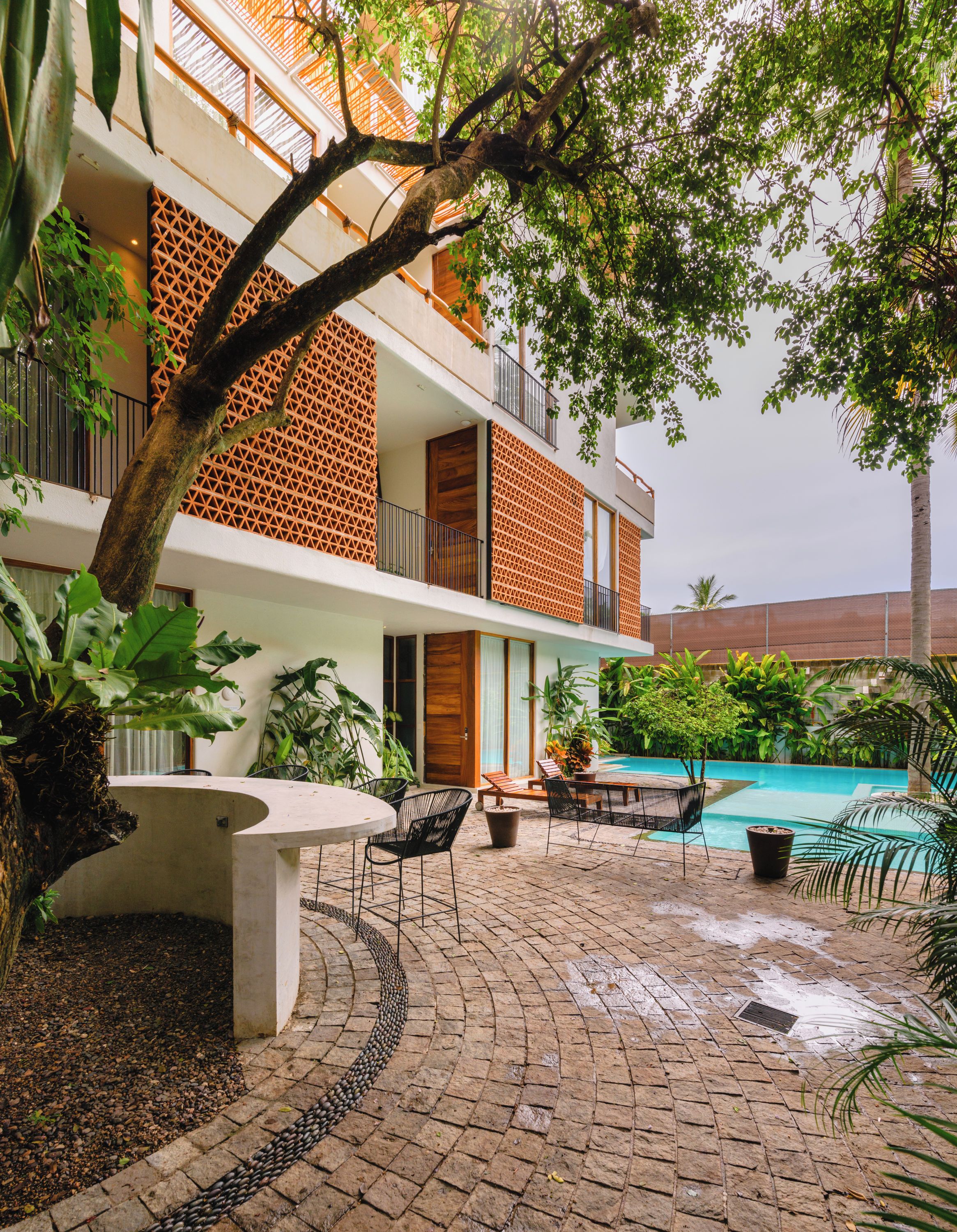 A multi-story building with a pool, outdoor seating, and lush greenery.