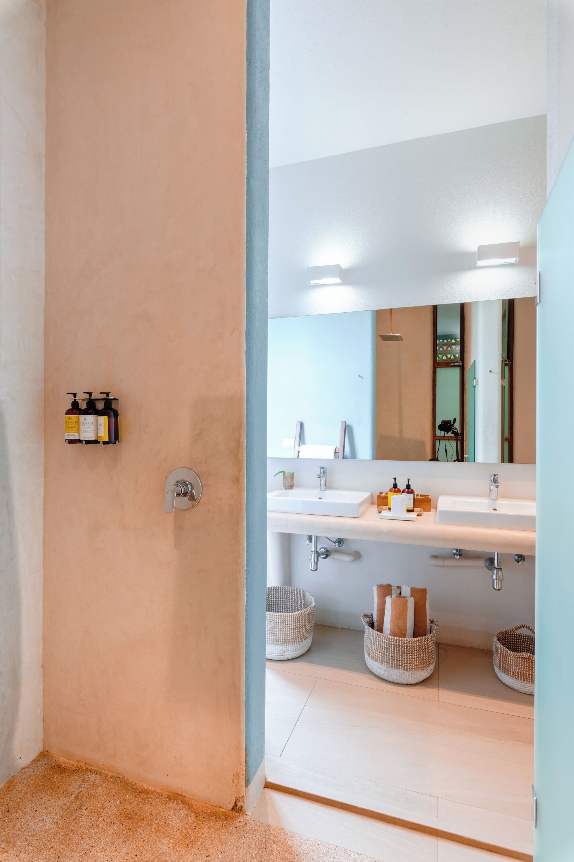 A bathroom with two sinks, a mirror, and three baskets on the floor.