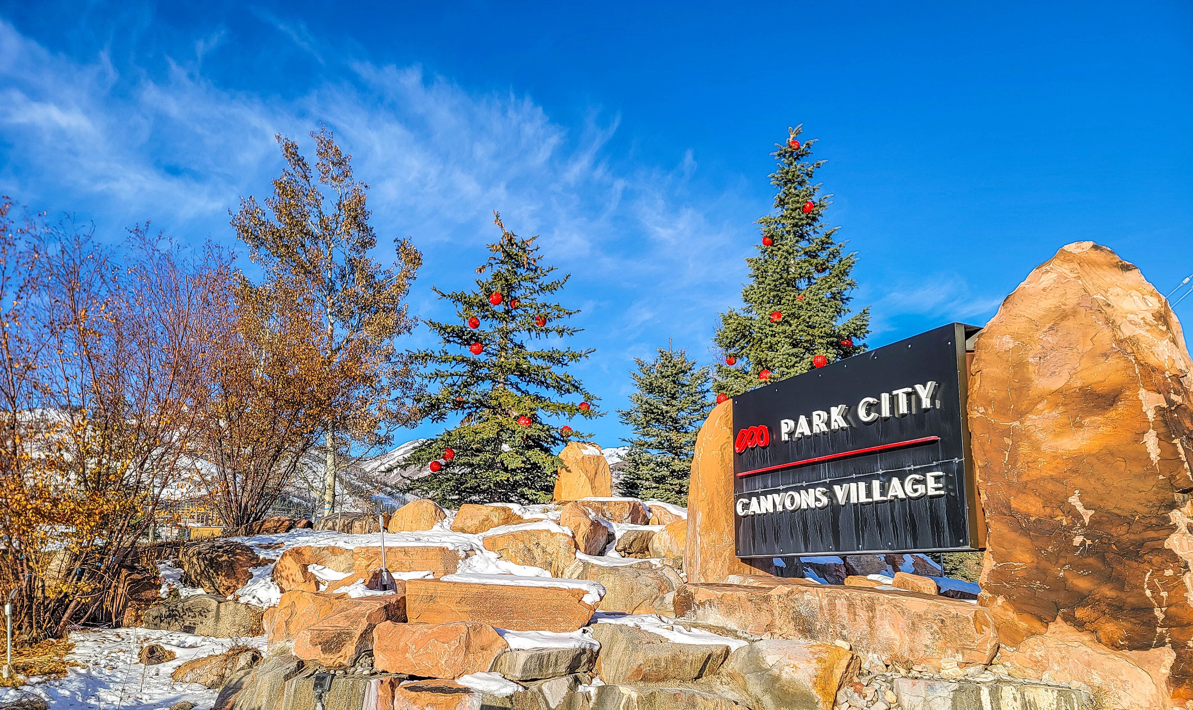 A sign for Park City Canyons Village with a clear blue sky and snow-covered ground.