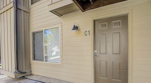 Un bâtiment de couleur beige, avec une porte marquée « C1 » et une fenêtre équipée de stores.