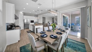 A modern kitchen with white cabinets, a stainless steel refrigerator, and a dining area with a wooden table set for four. - ⭐⭐⭐⭐⭐ ⭐Heated Pool & Spa, Gourmet Kitchen, Game Room, Fire Table & BBQ Island  (Mesa)