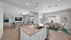A spacious kitchen with a central island, dining area with chairs, and a TV mounted on the wall. - ⭐⭐⭐⭐⭐ ⭐Heated Pool & Spa, Gourmet Kitchen, Game Room, Fire Table & BBQ Island  (Mesa)