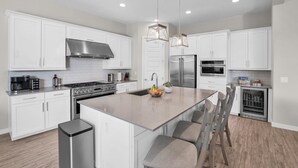 A modern kitchen with white cabinetry, stainless steel appliances, a central island with seating, and pendant lighting. - ⭐⭐⭐⭐⭐ ⭐Heated Pool & Spa, Gourmet Kitchen, Game Room, Fire Table & BBQ Island  (Mesa)