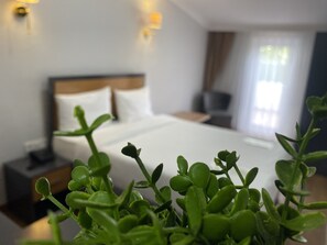 A hotel room with a neatly made bed, a bedside table, and a potted plant in the foreground. - Airport İnalens Konaklama (Arnavutköy)