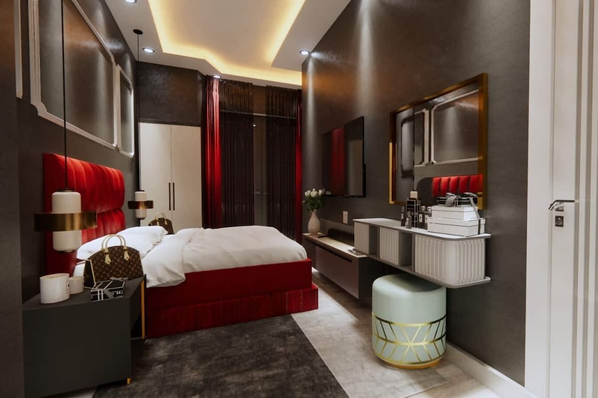 Une chambre moderne avec un grand lit, une coiffeuse avec un miroir et un mur d’accent rouge.