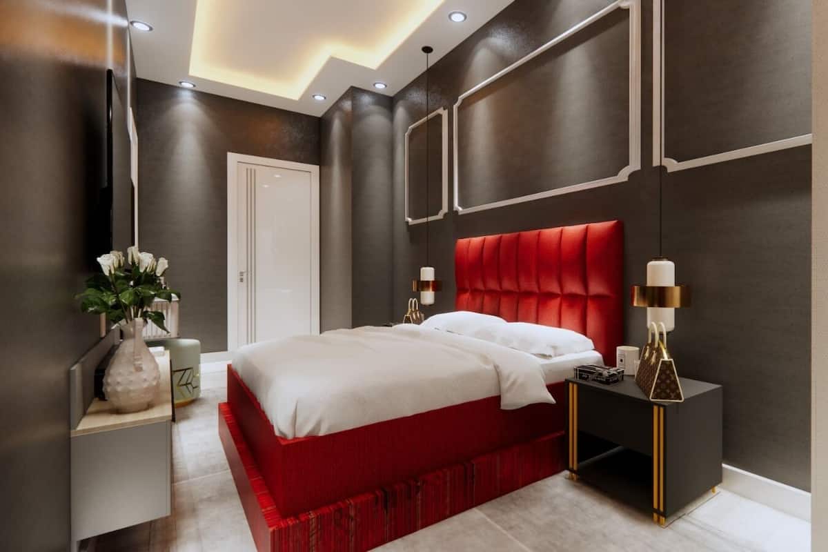 Une chambre à coucher moderne avec un lit recouvert d’un tissu rouge, une table de chevet blanche et une petite table noire avec une lampe.