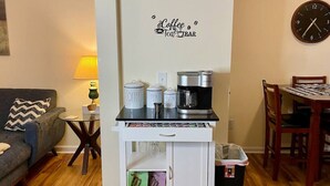 En kompakt opholdsstue med et tekøkken, kaffestation, spiseplads og sofa.