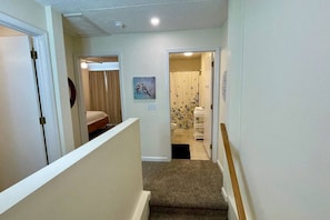 A hallway with a carpeted staircase leading to a bedroom with a bed and a painting on the wall.