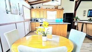 A kitchen with wooden cabinets, a microwave, and a sink. There is a dining table with chairs and a vase with flowers. - CAPTAIN'S CAPTAIN-Waterfront House (Port Arthur)
