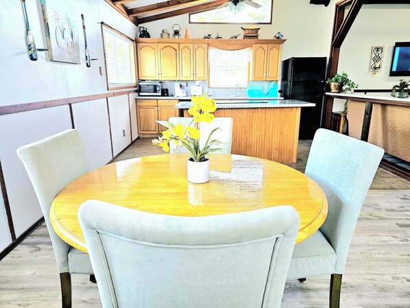 A kitchen with wooden cabinets, a microwave, and a sink. There is a dining table with chairs and a vase with flowers. - CAPTAIN'S CAPTAIN-Waterfront House (Port Arthur)