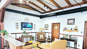 A cozy living room with a wooden ceiling, a television, a sofa, a chair, and a small table with a plant. - CAPTAIN'S CAPTAIN-Waterfront House (Port Arthur)