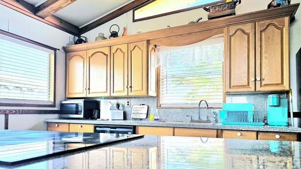 A kitchen with wooden cabinets, a granite countertop, a microwave, a coffee maker, and a teal-colored coffee machine. - CAPTAIN'S CAPTAIN-Waterfront House (Port Arthur)