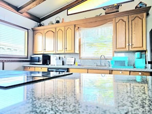A kitchen with wooden cabinets, a granite countertop, a microwave, a coffee maker, and a teal-colored coffee machine.